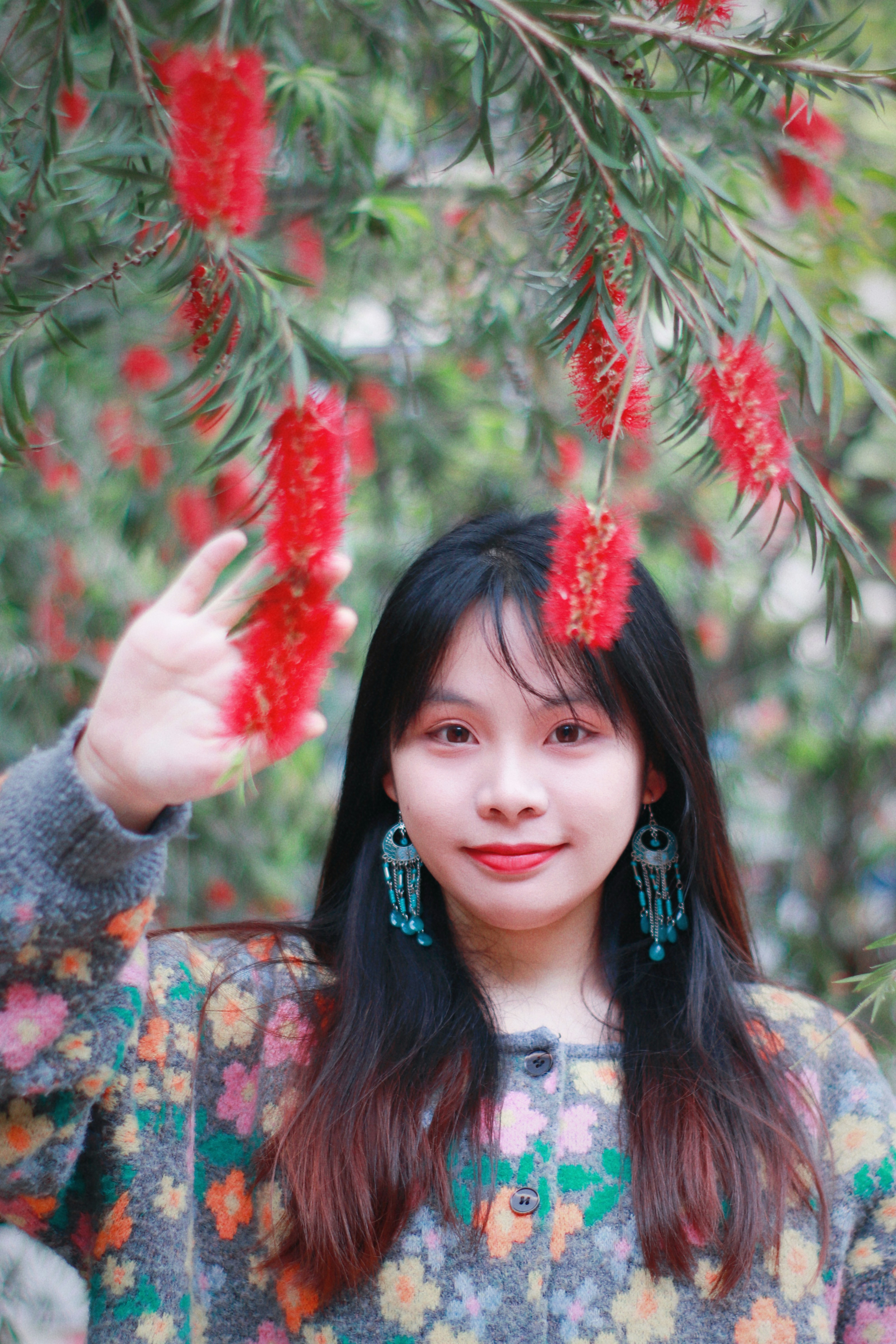 woman with dangly blue earings underneath a red flower drapping tree