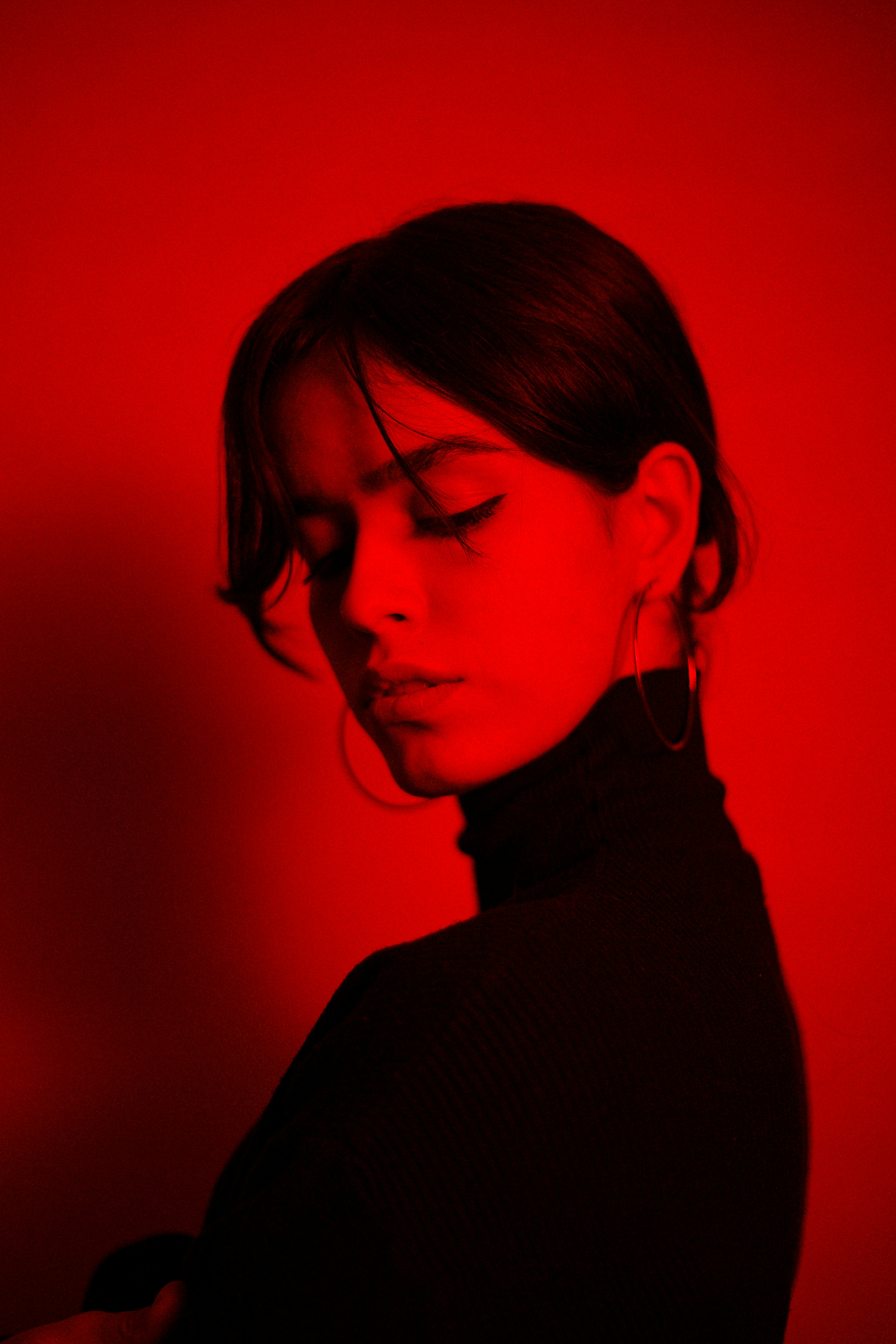 woman, red background , wearing large hoop earings and a turtle neck top