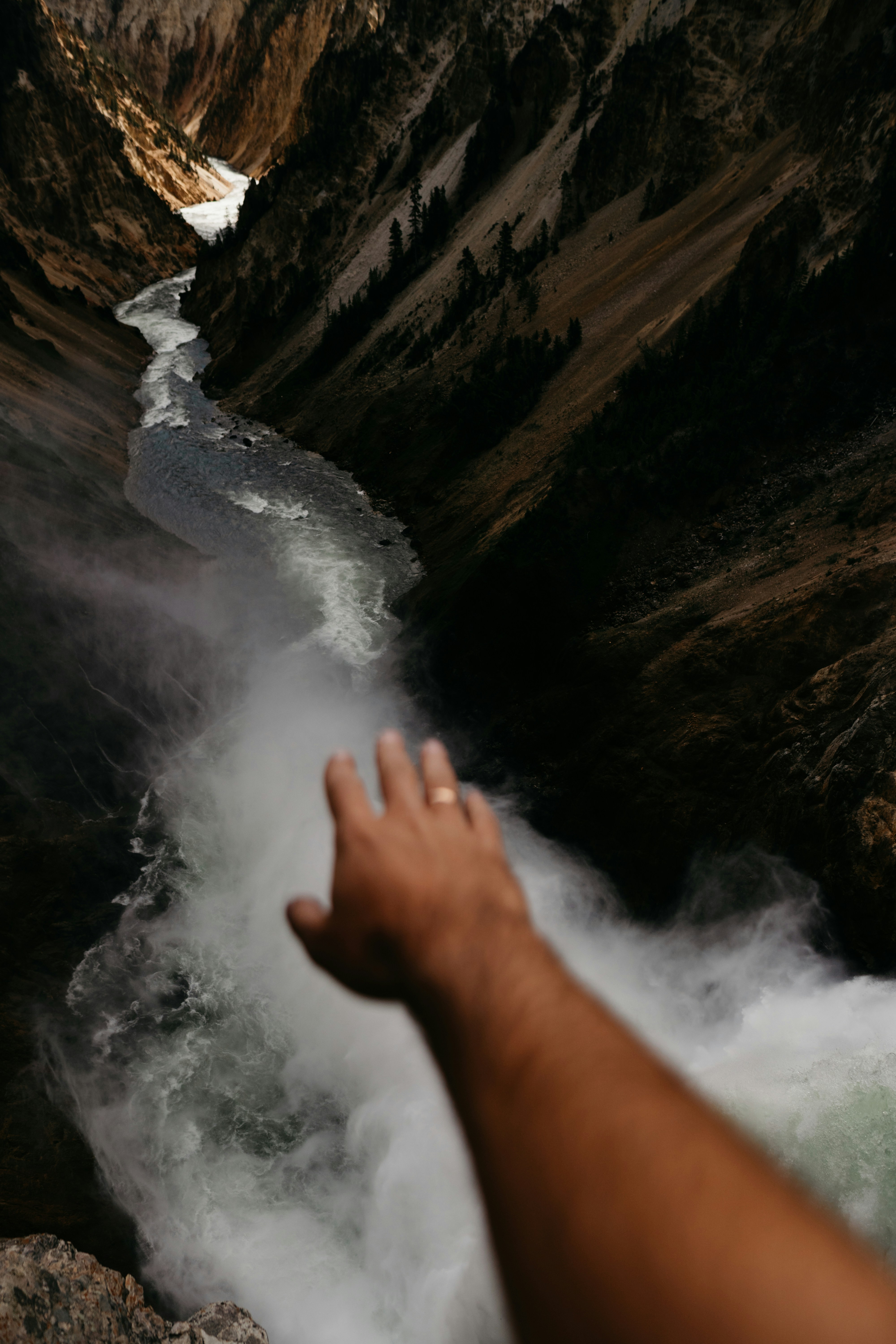 hand reaching out towards river from high about the water at the cliff mouth. wearing a ring